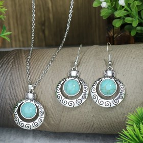 Resim Bir çift küpe ve bir kolyeden oluşan, metal yüzeyinde oyma tasarım ve kakma sentetik turkuaz bulunan, günlük kullanım veya partiler için uygun, kadınlar için tasarlanmış vintage bir takı seti. 